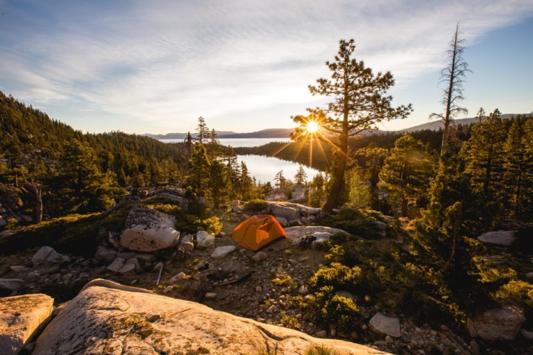 beautiful-shot-orange-tent-rocky-mountain-surrounded-by-trees-during-sunset.jpg